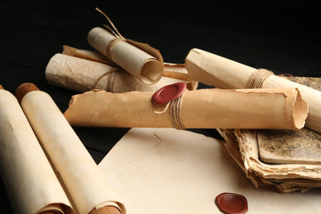 Many old rolled scrolls on black wooden table, closeup