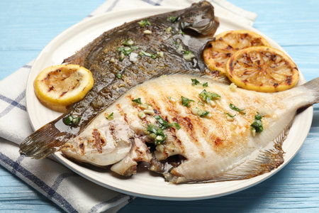 Tasty roasted flounder fish with herbs and lemon slices on light blue wooden table, closeup. Homemade seafood dishの写真素材