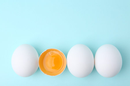 Whole and broken chicken eggs on light blue background, top view. Space for text