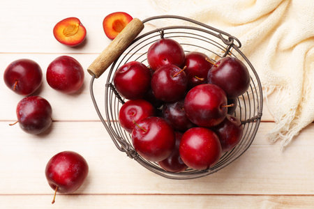 Ripe cherry plums and metal basket on light wooden table, flat lay