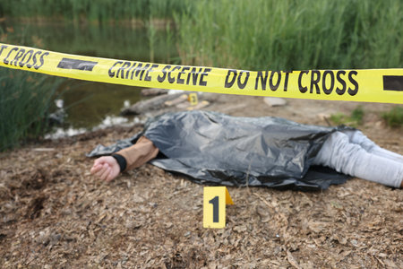 Forensic expertise. Crime scene with dead man's body, marker and police tape near lake outdoors, selective focusのeditorial素材