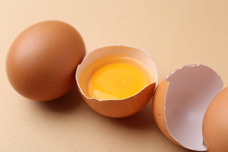 Whole and broken chicken eggs on beige background, closeup
