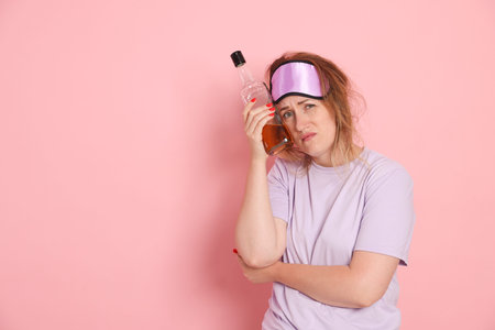 Woman with bottle of alcoholic drink suffering from hangover on pink background. Space for textの写真素材