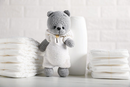 Baby diapers, shampoo and toy bear on white table near brick wall