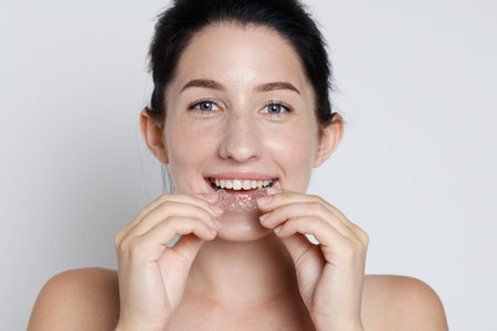 Portrait of smiling woman wearing dental aligner on grey background, closeup
