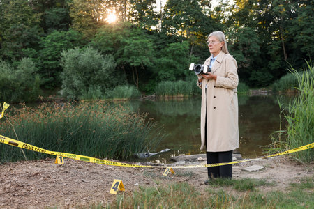 Forensic expertise. Detective with camera working at crime scene near lake outdoors, space for text