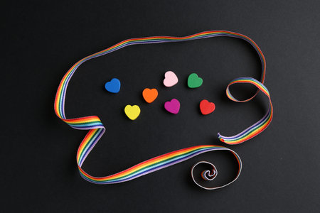 Tolerance concept. Colorful hearts and ribbon on black background, flat lay