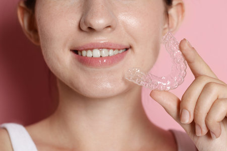 Smiling woman with dental aligner on pink background, closeup