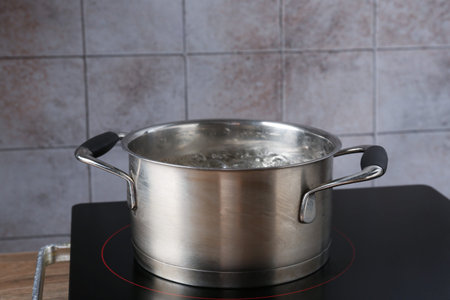 Metal pot with boiling water on stove in kitchen, closeup