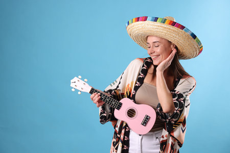Happy woman in sombrero hat with ukulele on light blue background. Space for text