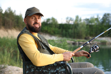 Fisherman with rod sitting on chair and fishing near lake at summerの写真素材