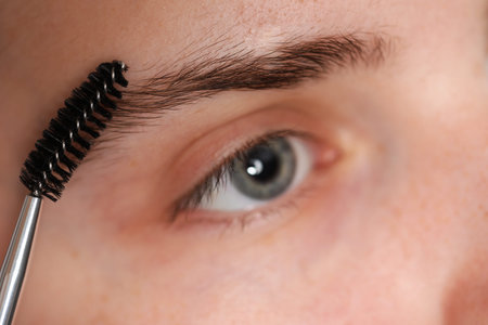 Young woman brushing her eyebrow with spoolie, closeup