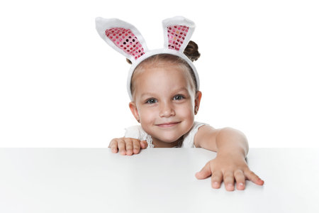 Curious little girl in bunny ears peeking over table against white background