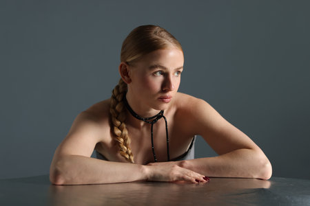 Beautiful woman with pigtail posing at table on gray backgroundの写真素材