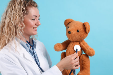 Pediatrician checking heartbeat of toy bear on light blue backgroundの写真素材