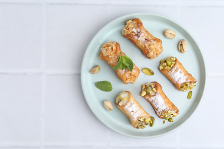 Delicious cannoli with nuts and mint on white tiled table, top view. Space for text