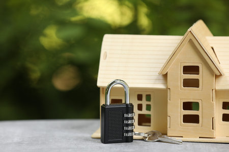 Home security. House model, key and padlock on light grey table outdoors, closeup. Space for text