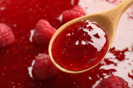 Delicious raspberry jam with fresh berries and spoon as background, closeup