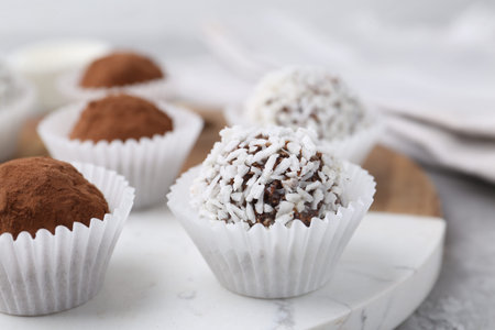 Homemade candies with cocoa powder and coconut flakes on table, closeup
