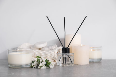 Spa composition with burning candles and reed diffuser on light grey table