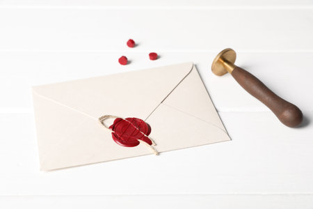 Envelope with wax seal and stamp on white wooden table, closeup