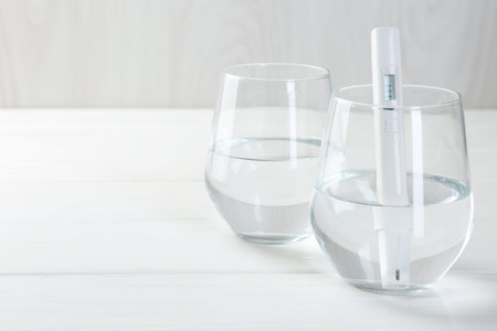 Nitrate tester in glass of water on white wooden table, closeup. Space for text