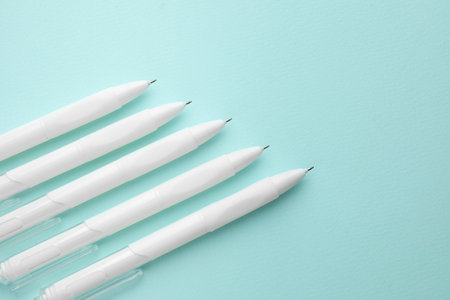 White pens on light blue background, flat lay. Space for text
