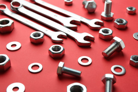 Metal wrenches, nuts and bolts on red background, closeup