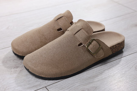 Stylish beige slippers on light wooden floor, closeup