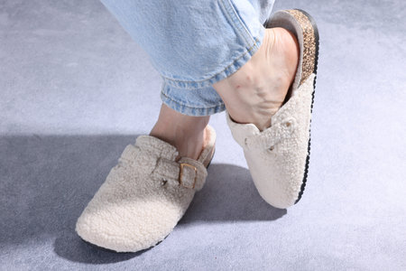 Woman in stylish white slippers on grey textured floor, closeup