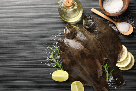 Fresh flounder fish, salt and products on black wooden table, flat lay with space for text. Raw...