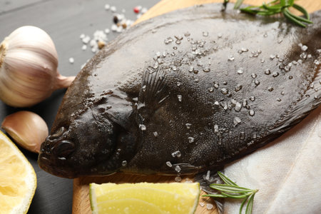 Fresh raw flounder fish and spices on black wooden table, closeup. Seafood