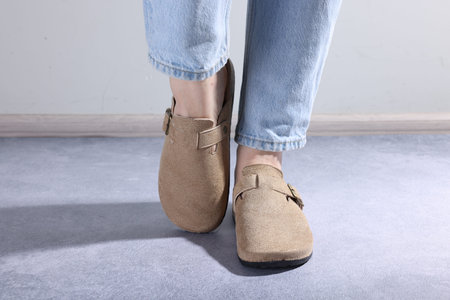 Woman in stylish beige slippers on grey textured floor, closeup