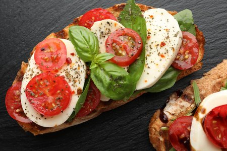 Delicious sandwiches with mozzarella cheese, tomatoes and basil on black table, flat layの写真素材