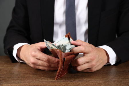 Man with dollars in wallet at wooden desk, closeup