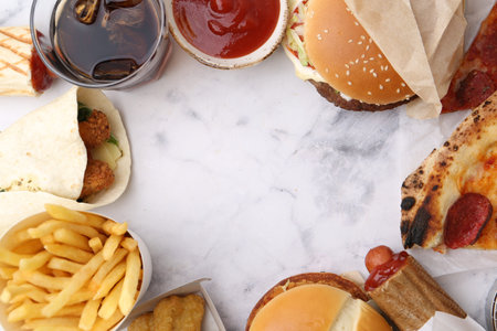 Different fast food and soda drink on white marble table, flat lay. Space for text