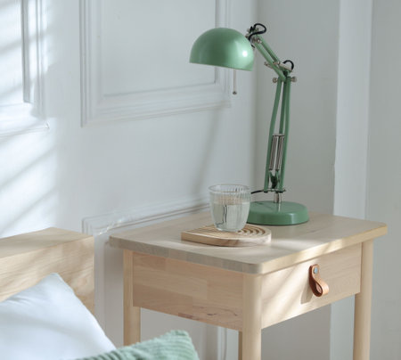 Bedside table with lamp and glass of water near bed indoors