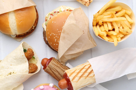 Different delicious fast food on white tiled table, flat lay