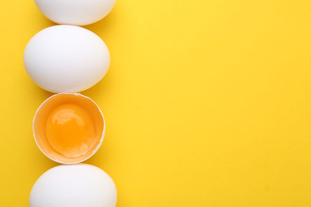 Whole and broken chicken eggs on yellow background, top view. Space for text
