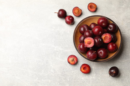 Ripe cherry plums and bowl on gray textured table, flat lay. Space for text