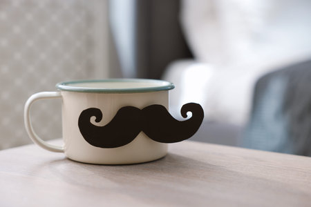 Happy Father's Day. Cup with mustache on wooden table at home, closeup. Space for text