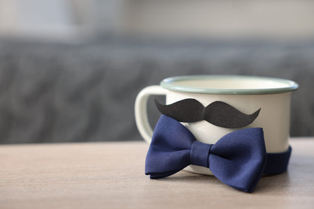 Happy Father's Day. Cup with mustache and bowtie on wooden table at home, closeup. Space for textの写真素材