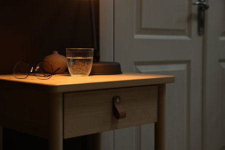 Wooden side table with glass of water and glasses near brown wall indoors, closeupの写真素材