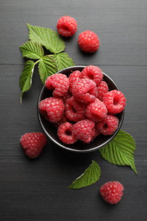 Tasty fresh ripe raspberries and leaves on black table, flat lay