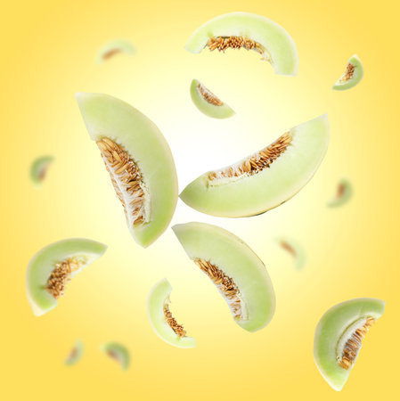 Cut fresh ripe melons swirling in air against yellow gradient backgroundの写真素材