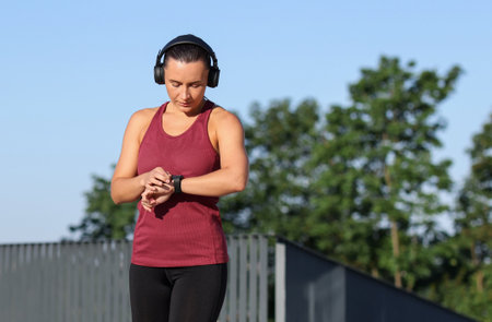 Athletic young woman with headphones checking fitness tracker before running outdoors, space for textの写真素材