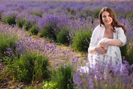 Beautiful young woman sitting among lavender flowers outdoorsの写真素材
