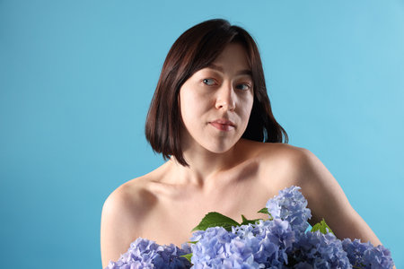Beautiful young woman with hortensia flowers on light blue backgroundの写真素材