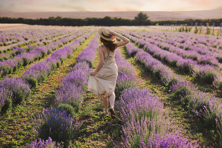 Woman with straw hat and beautiful flowers running through lavender fieldの写真素材