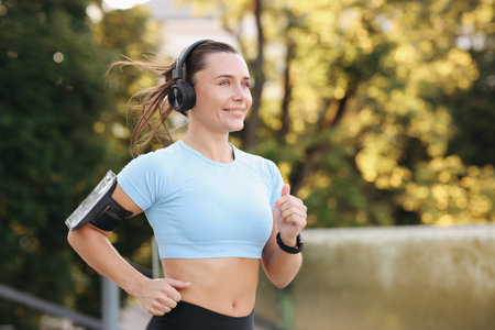 Athletic young woman with headphones running outdoors, space for textの写真素材